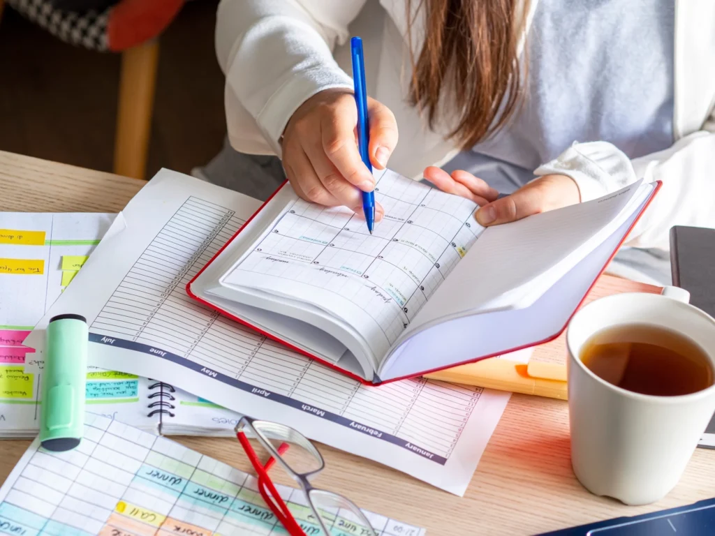 Woman sitting at a table writing in a weekly planner next to a cup of tea